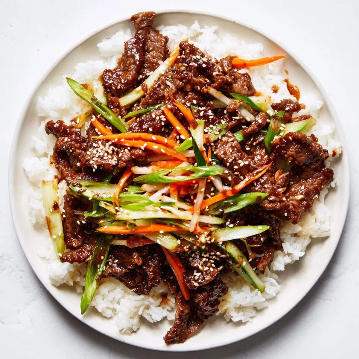 Steaming white rice is topped with savory bulgogi beef bowl, garnished with fresh scallions and sesame seeds.