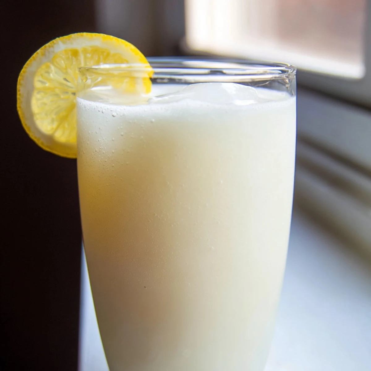 A tall glass of creamy lemonade, filled with ice cubes and garnished with fresh lemon slices and mint leaves.  