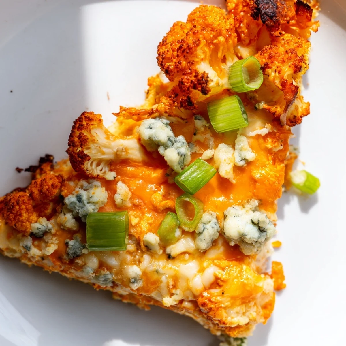 Slices of Buffalo Cauliflower Pizza topped with celery and blue cheese crumbles served on a white plate with napkin.