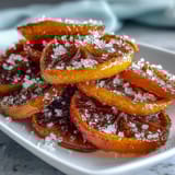 Candied orange slices for cocktail garnish, glistening with sugar syrup and arranged on a rustic wooden board.