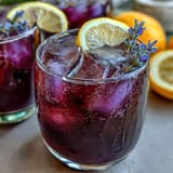 A refreshing purple lemonade with lavender, citrus, and grape juice, served over ice with lemon slices.
