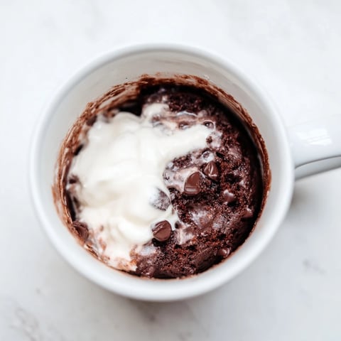 Steaming hot chocolate mug cake topped with whipped cream, ready for a quick dessert.