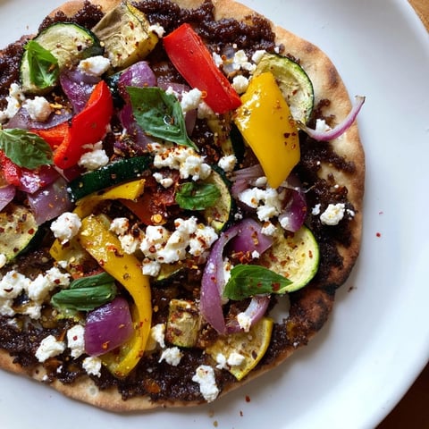 Image of a naan bread pizza baked to golden perfection, loaded with vegetables and feta cheese.