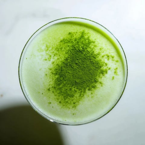 A frothy Matcha Martini cocktail, garnished with matcha powder, sits in a chilled martini glass ready to sip.