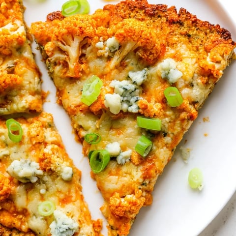 Golden-brown Buffalo Cauliflower Pizza with melted mozzarella, spicy red sauce, and fresh green onions on a rustic wooden board.