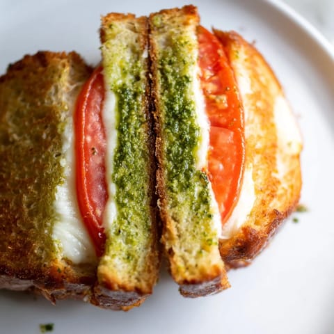 A vegetarian Caprese Pesto Grilled Cheese rests on a cutting board, showcasing melted mozzarella and ripe tomato slices between buttery, golden-brown bread.