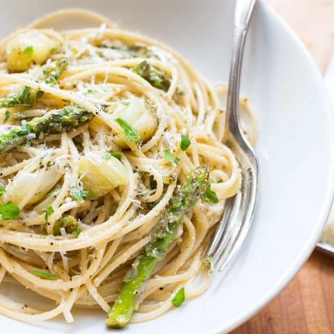 Close-up of Roasted Garlic & Asparagus Pasta twirled on a fork, showing silky Parmesan sauce and fresh parsley garnish.