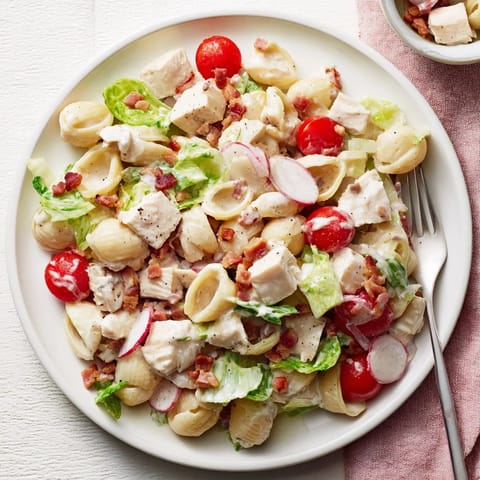 Hearty BLT Chicken Pasta Salad with tender shells, golden grilled chicken, and fresh veggies, served on a rustic plate.  