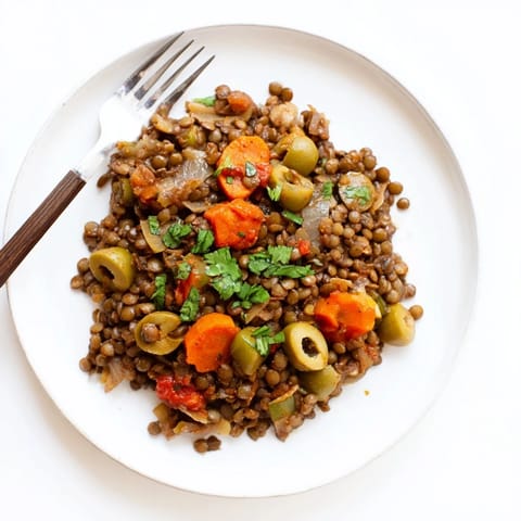 A close-up of vibrant Cuban-Inspired Lentil Picadillo, featuring tender lentils, green olives, and golden raisins in a rich tomato sauce.  