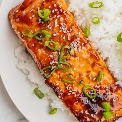 Golden-brown Maple Soy Glazed Salmon fillets resting on fluffy jasmine rice beside crisp broccoli and snap peas.  