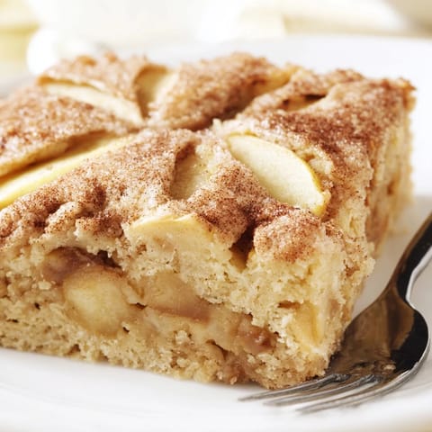 Golden baked apple cake casserole with tender apples and cinnamon topping, sliced and served on a wooden board for a comforting treat.