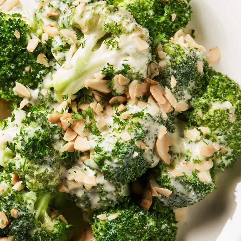 A bowl of vibrant broccoli salad featuring a tangy garlic Parmesan dressing, red onion, and cherry tomatoes, served as a light lunch.