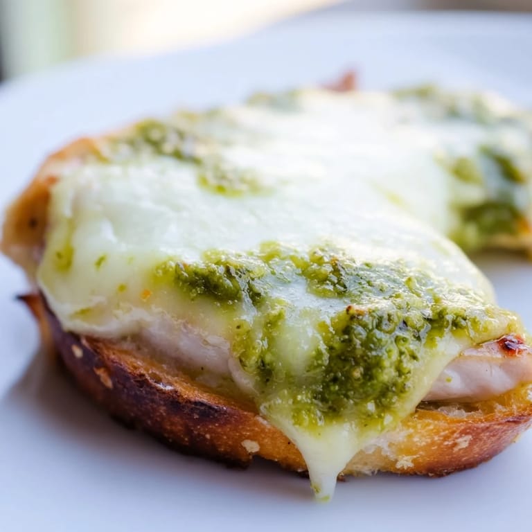 A close-up of the Pesto Chicken Melt sandwich showing gooey cheese, vibrant green pesto, and juicy grilled chicken inside crispy bread.