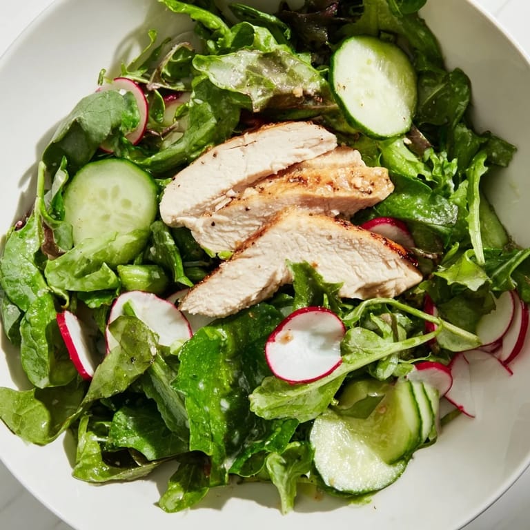 A close-up of Spring Detox Chicken Salad showing sliced grilled chicken, vibrant greens, cucumber, and radish, garnished with lemon wedges for a low-carb meal.