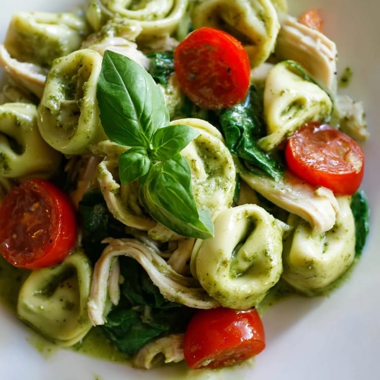 Serving suggestion for creamy pesto tortellini skillet: fresh basil leaves and grated Parmesan on top.